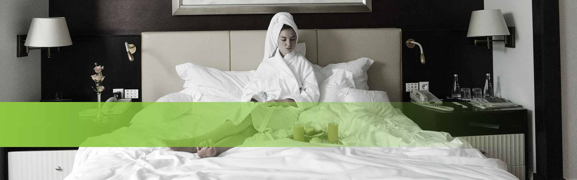 Kategorie Unterkünfte - Frau im Bademantel sitz auf einem Hotelbett